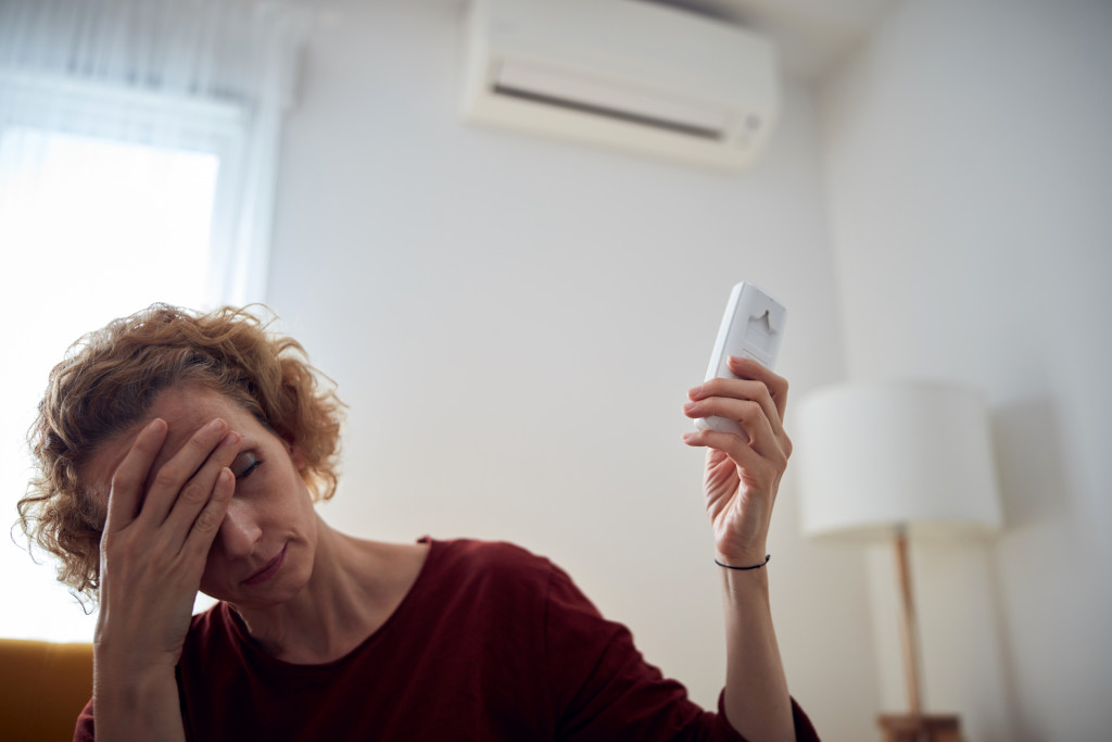 A woman with a headache changing the temperature of her air conditioner at home