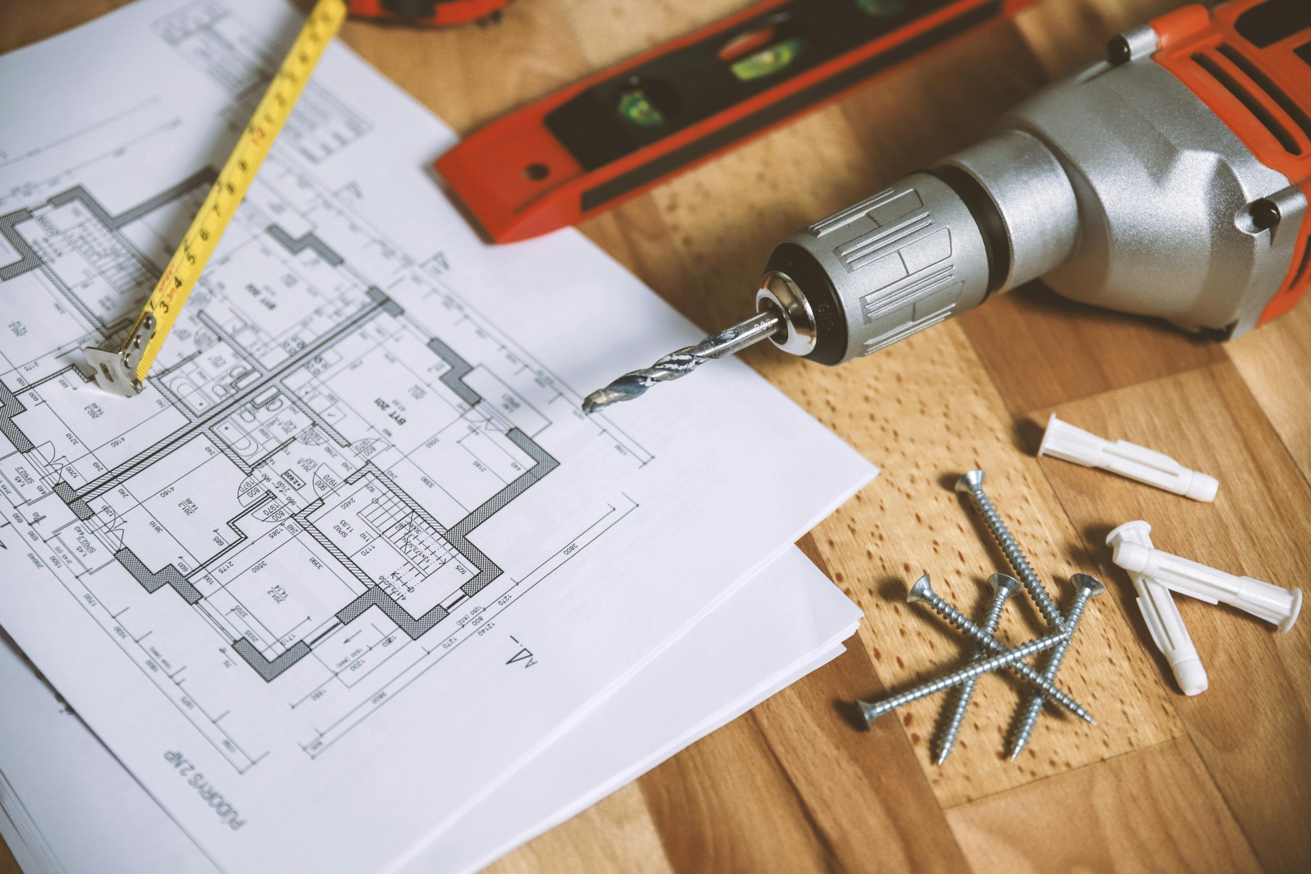 copy of a house blueprint laid out with a drill, measuring tape, and screws nearby