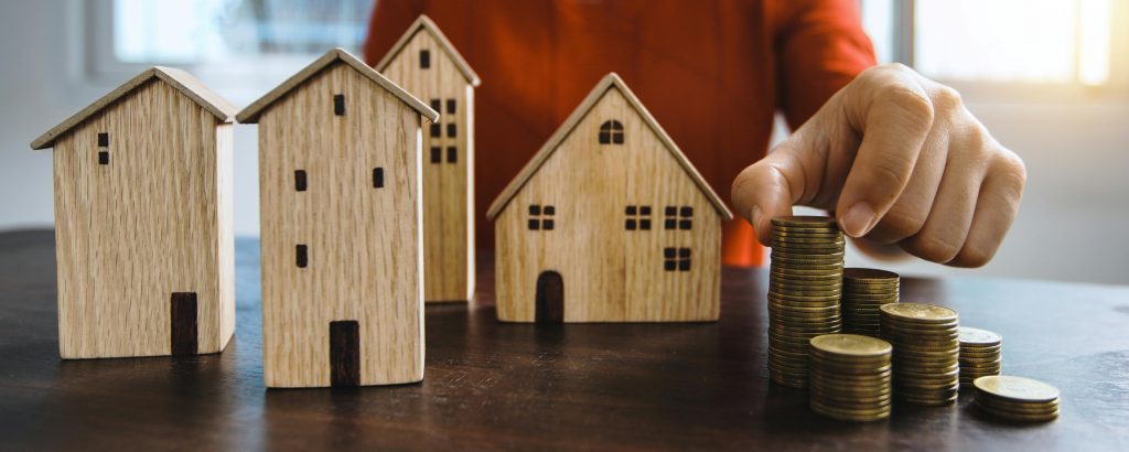hand stacking coins next to small wooden model houses