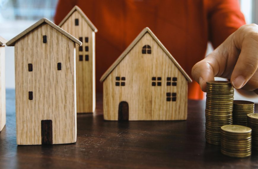hand stacking coins next to small wooden model houses
